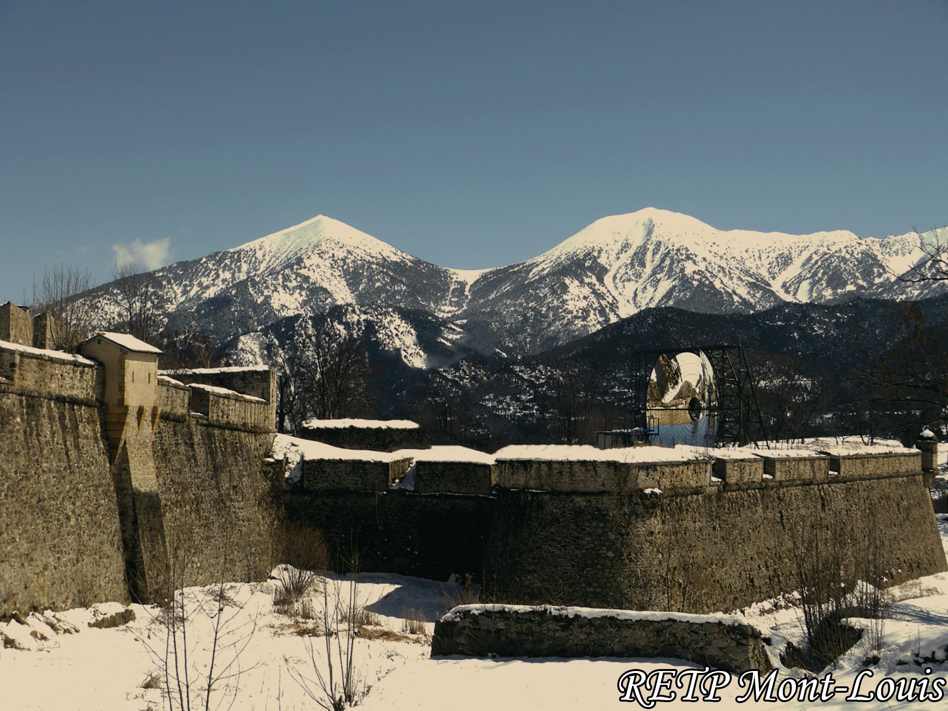 Le four solaire de mont louis en grand angle de face avec le col mitja enneige en arriere plan